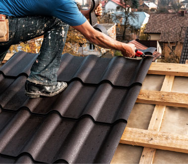 The image shows a construction worker installing a roof on a house during daylight hours.