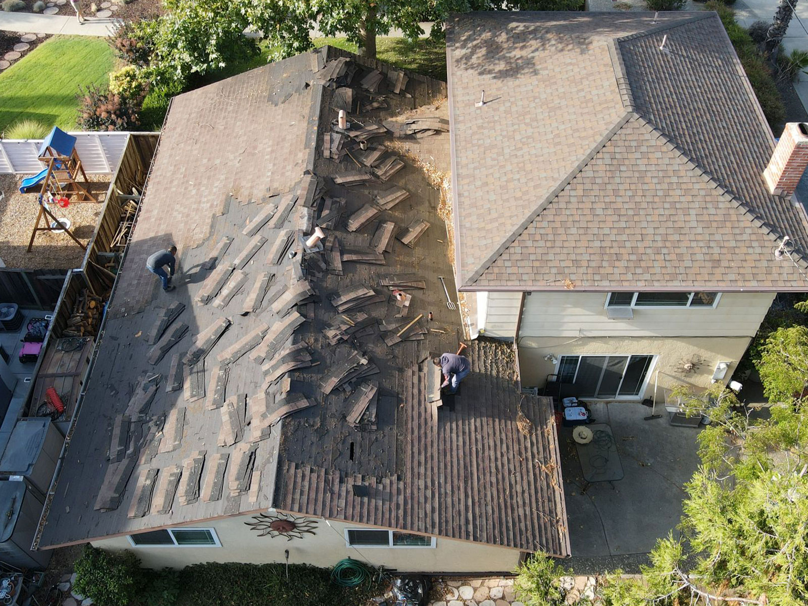 The image shows a residential house with a severely damaged roof under repair.