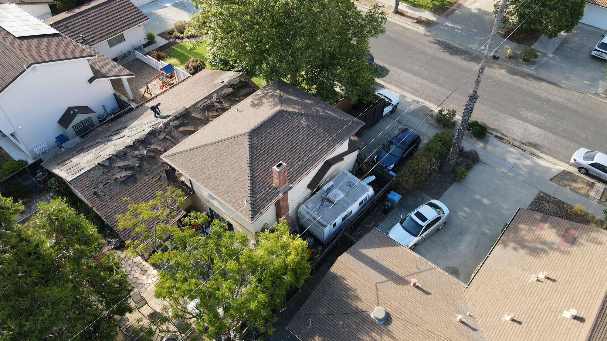 The image shows a residential street scene with houses on both sides, a tree-lined sidewalk, parked cars, and a clear sky.