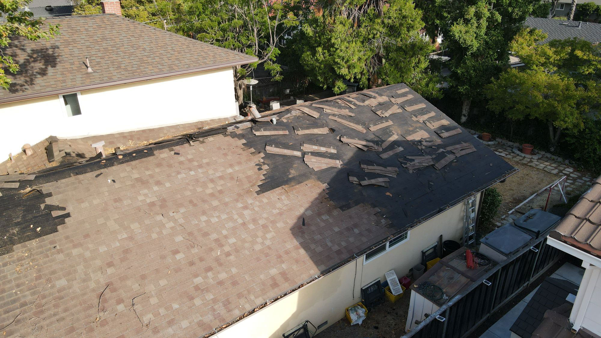 The image shows a residential house with a damaged roof, indicating recent hail damage, viewed from an angle that allows for a clear view of the affected area.