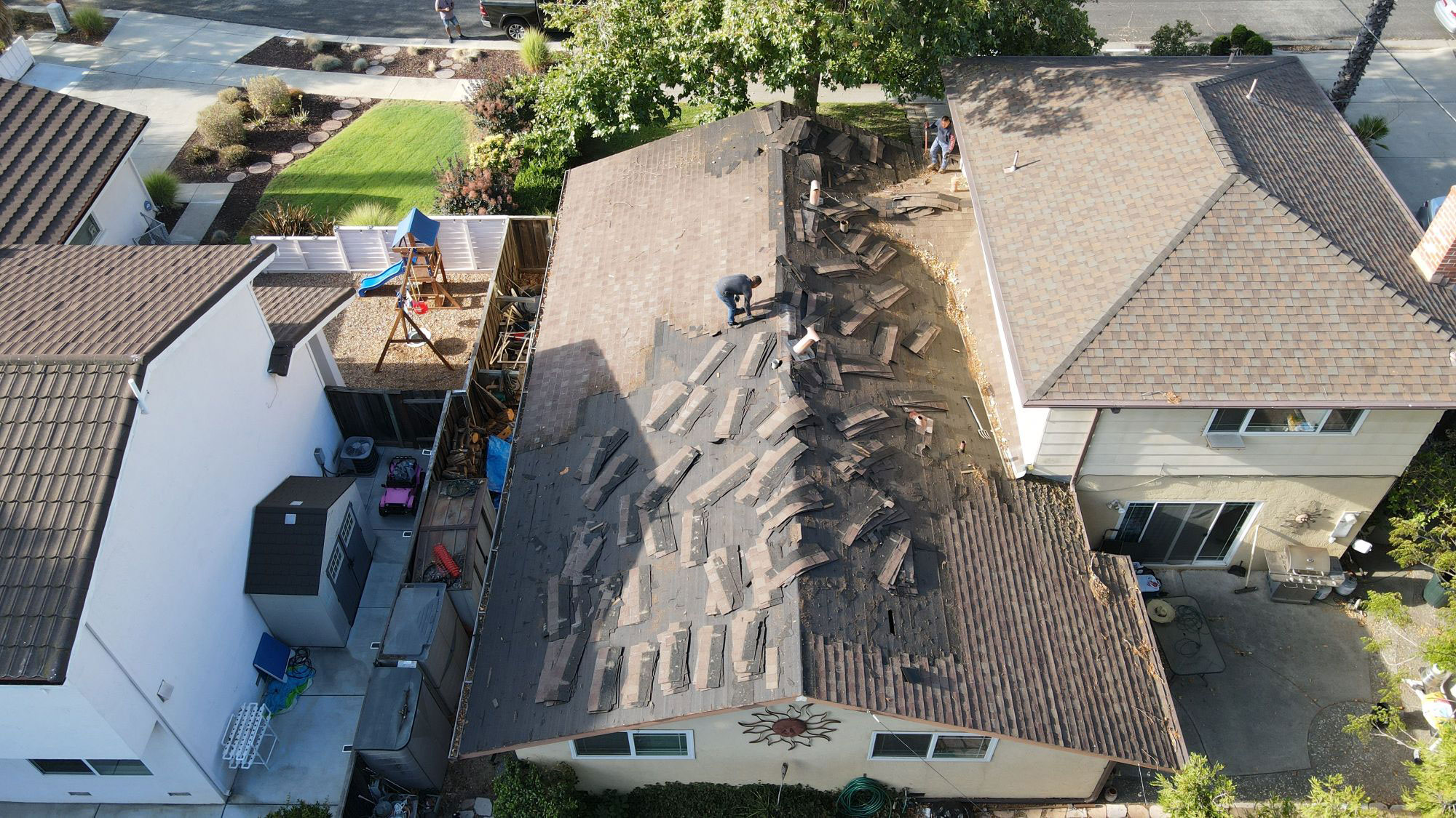 The image shows a residential property with a roof under repair or replacement, featuring workers on the roof and a visible progression of work from left to right.