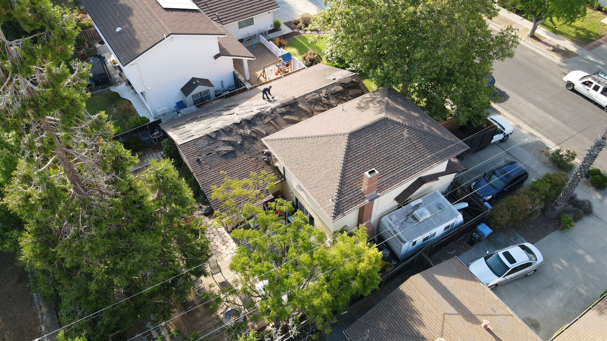 The image shows a residential house with visible roof damage, under a clear sky, viewed from an elevated angle.