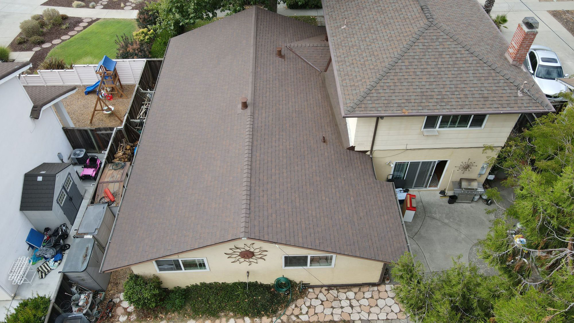 The image shows a two-story residential house with a brown roof, a garage, and a driveway.