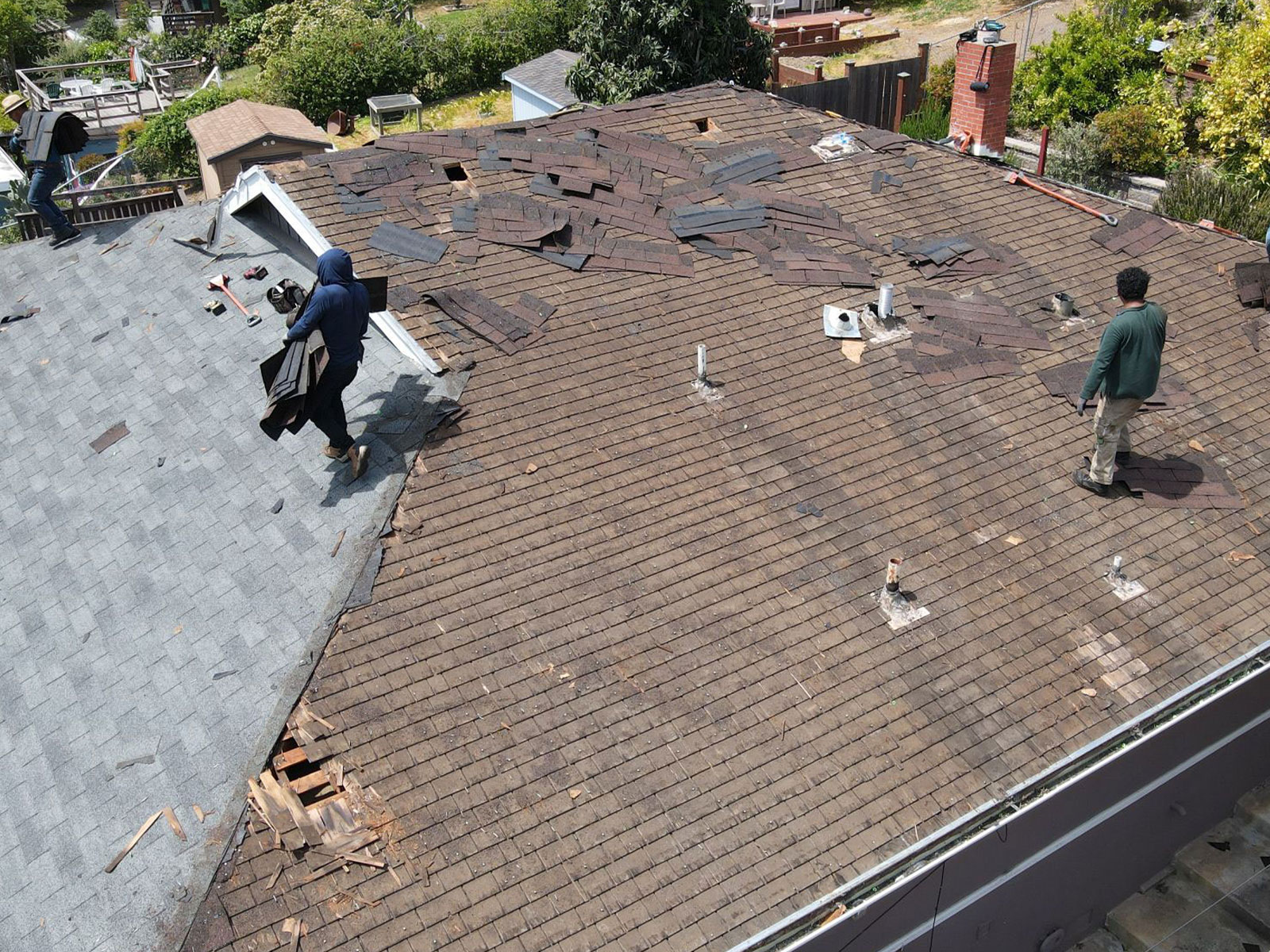 The image depicts a residential roof undergoing repair work, with two individuals visible, likely engaged in the renovation process.