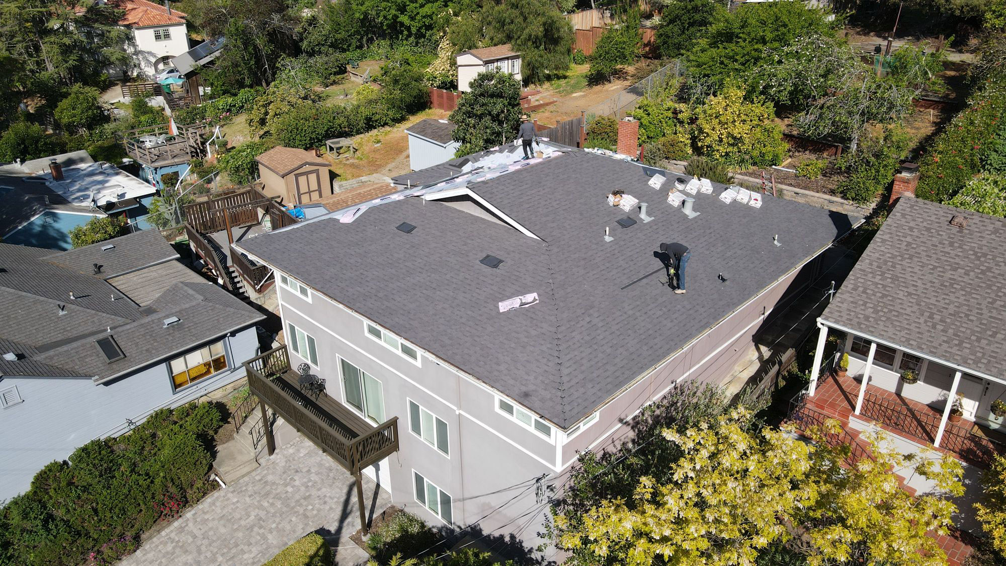 The image shows a residential house with a large grey roof, under construction with visible scaffolding and exposed areas where work is being done.