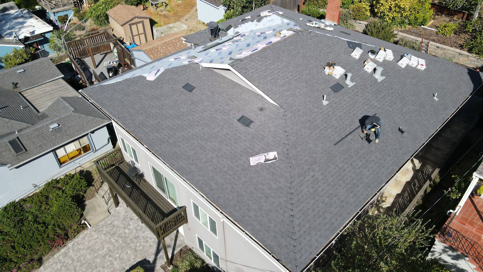 The image shows a residential house with a roof under construction or renovation, featuring visible materials such as shingles, flashing, and insulation.