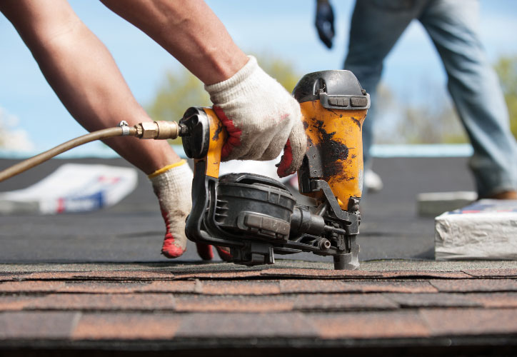 The image shows a construction worker using a power tool on a roofing job.