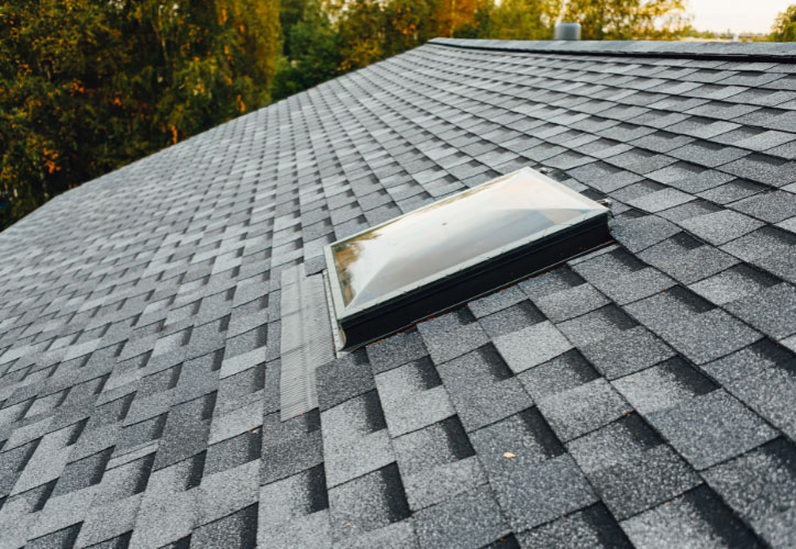 An image of a shingled roof with an open skylight window.