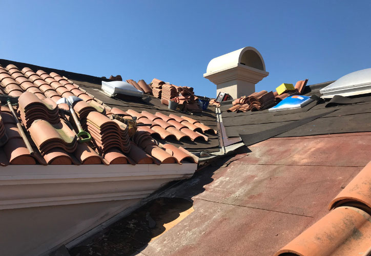 The image shows a roof with several damaged tiles and some missing, indicating recent damage or wear.