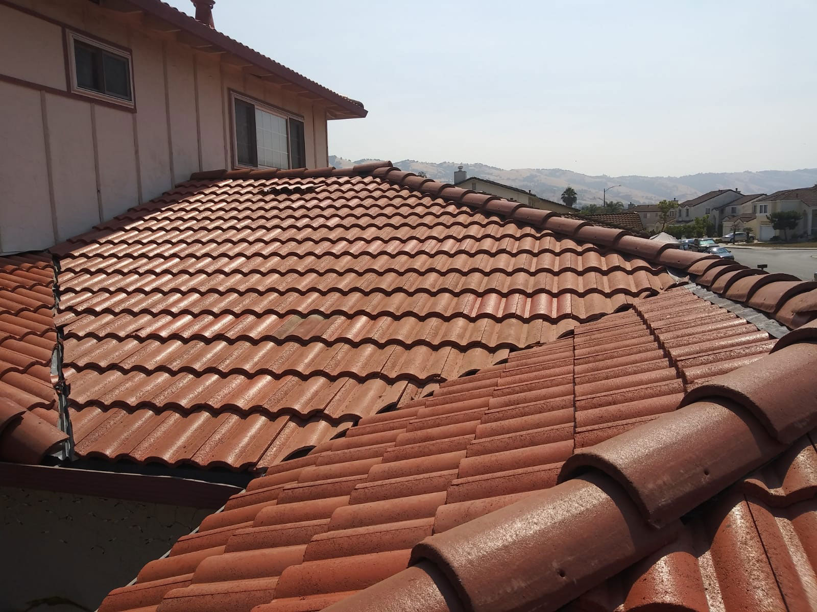 The image shows a residential building with a red clay tile roof partially covered by a metal gutter system.