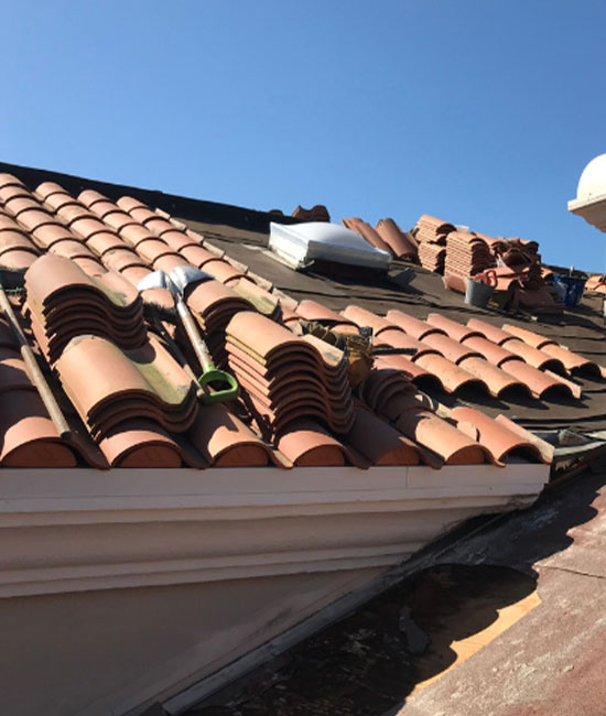 The image shows a section of a building with damaged roofing tiles, some of which have been removed and are scattered around.