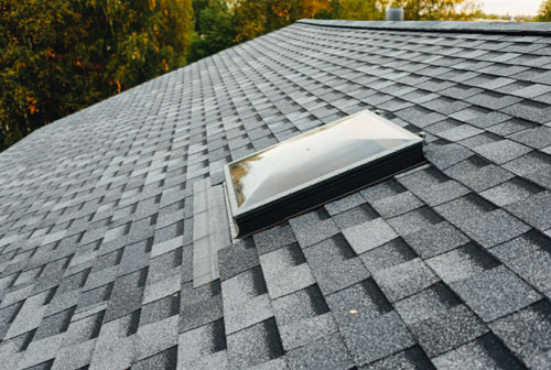 The image displays a close-up view of a dark roof with a skylight installed, showcasing its design and function.
