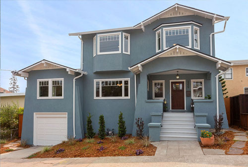 The image shows a two-story residential house with a white exterior, featuring a garage, front porch, and landscaping.